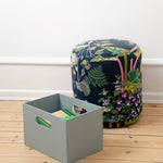 Gray storage box and floral-patterned ottoman on a wooden floor.