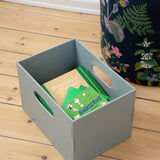 Gray storage box with green items on a wooden floor next to a floral-patterned bag.