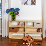 Wooden shelf with storage boxes and toys on a wooden floor, with a vase of flowers and a framed picture in the background.