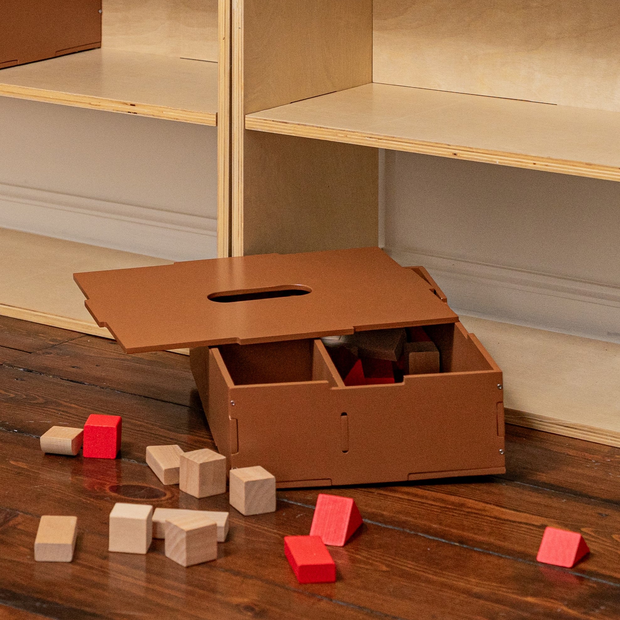 Cardboard box with cutouts on a wooden floor next to colorful blocks