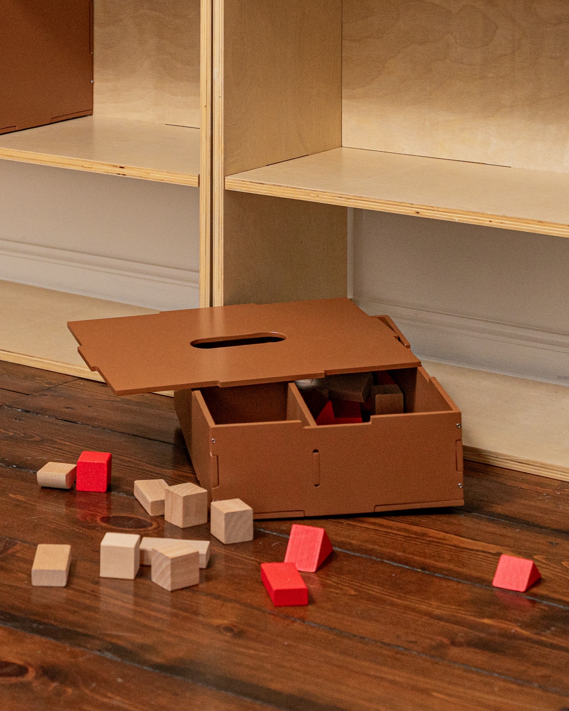 Cardboard box with cutouts on a wooden floor next to colorful blocks