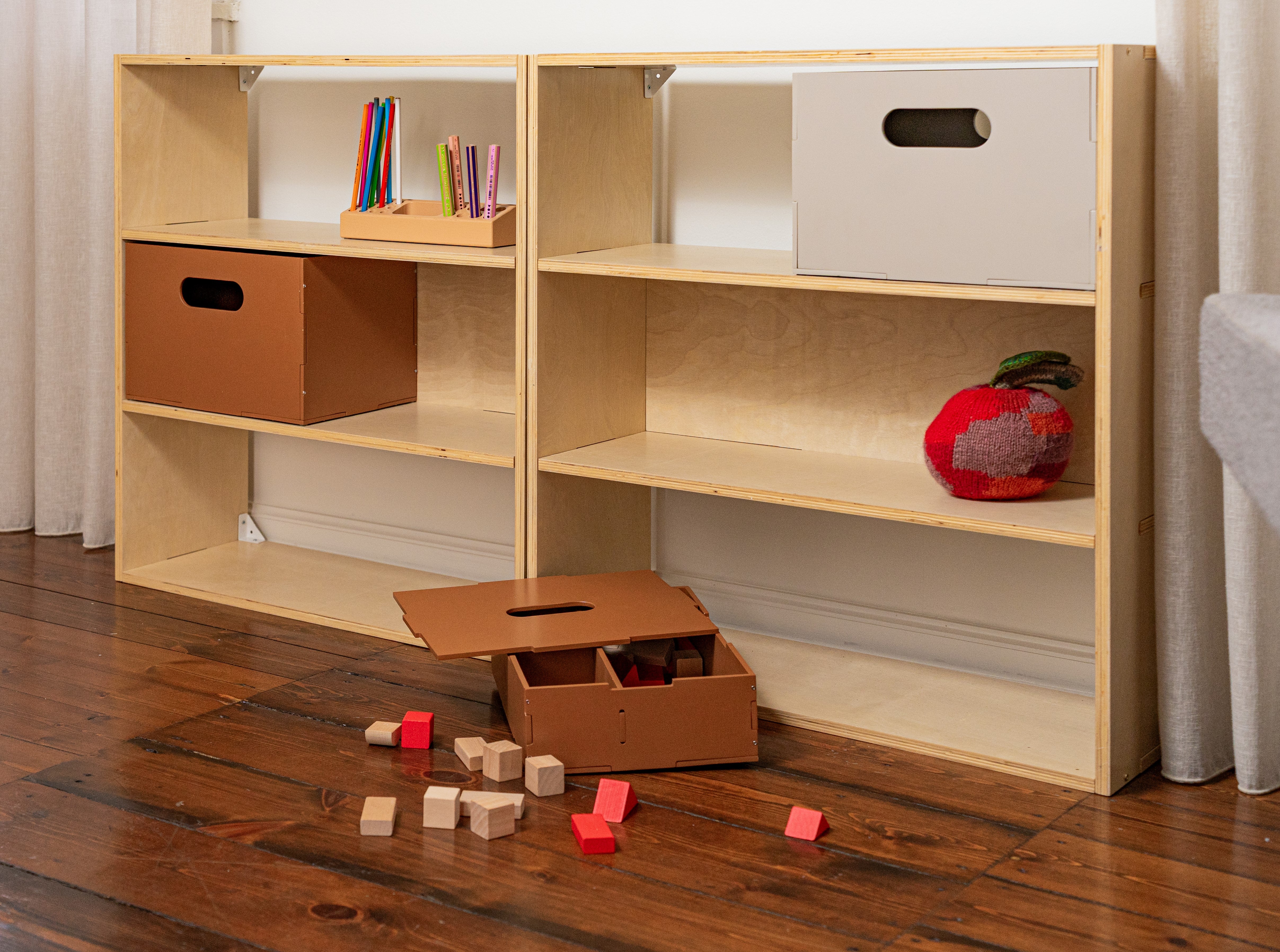 Wooden bookshelf with storage boxes and toys on a wooden floor.