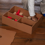 Child playing with wooden blocks inside a cardboard box on a wooden floor.