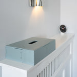 Light blue tissue box on a white surface with a clock in the background
