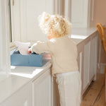 Child standing on a green stool reaching into a cabinet.