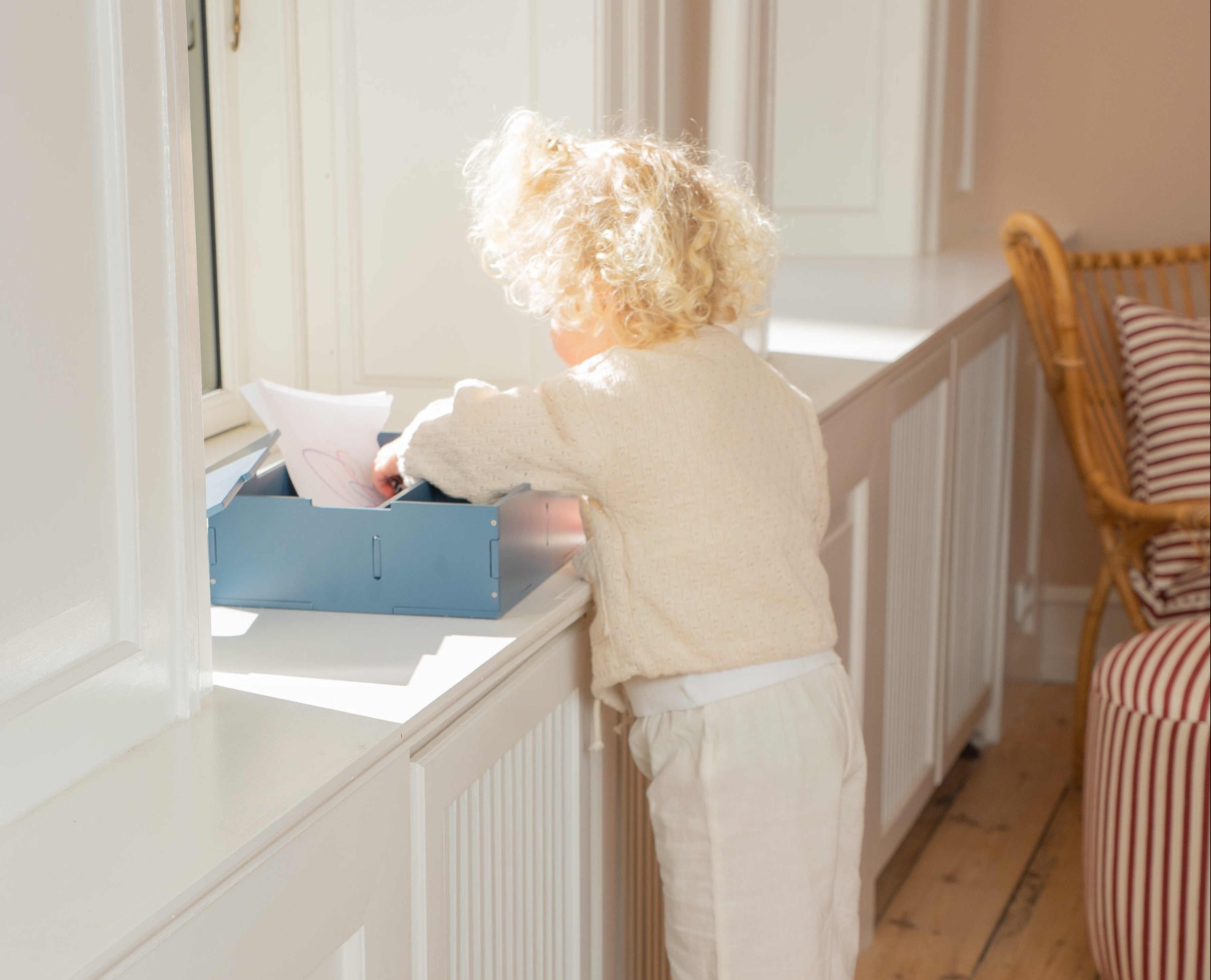 Child standing on a green stool reaching into a cabinet.