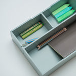 A light olive green wooden drawer organizer with three compartments, shown open and styled with colorful pencils, a ruler, and a notebook on a clean white background.