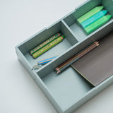 A light olive green wooden drawer organizer with three compartments, shown open and styled with colorful pencils, a ruler, and a notebook on a clean white background.