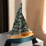 Model sailboat with a patterned green sail on a wooden base