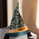 Model sailboat with a patterned green sail on a wooden base