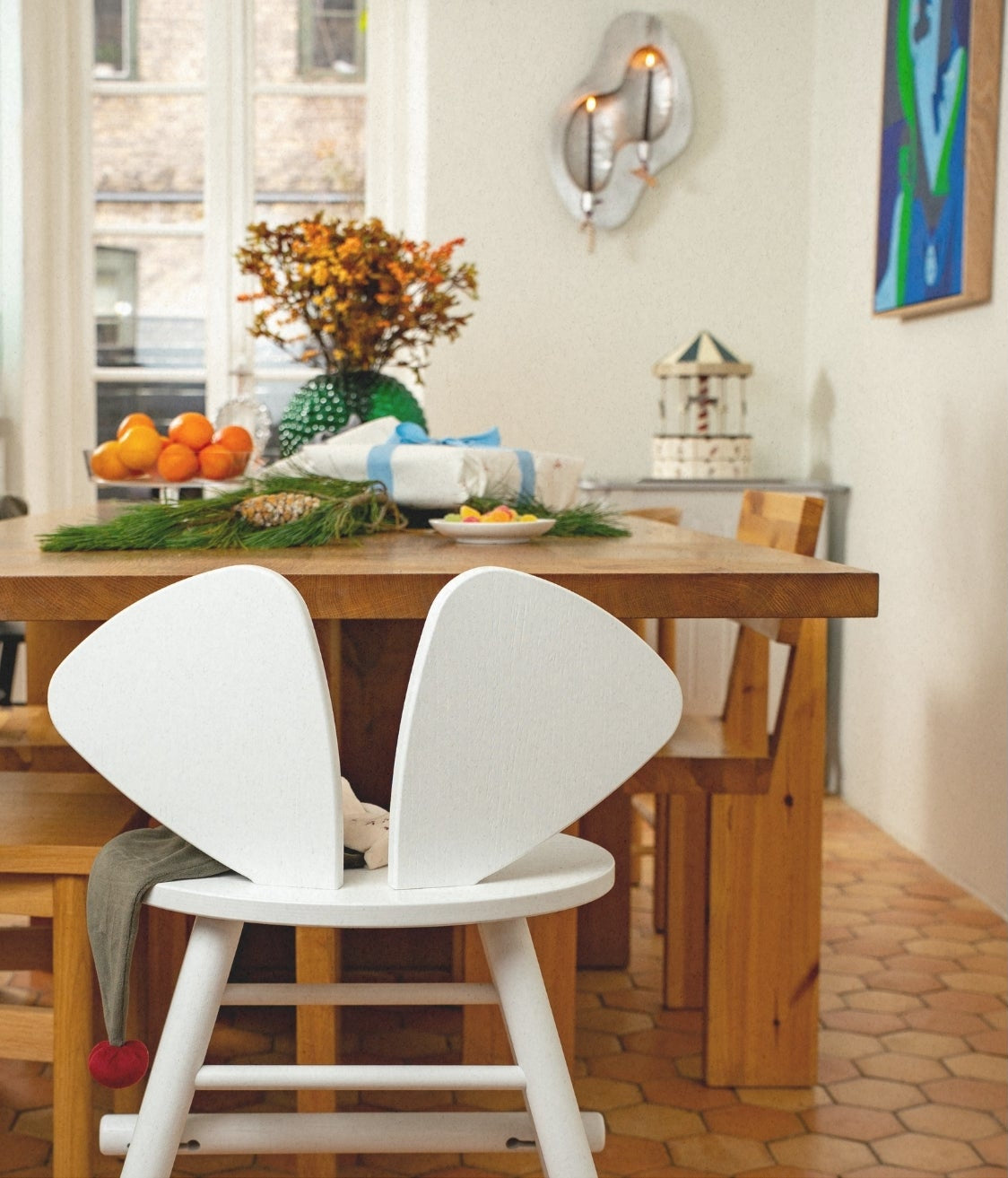Dining area with wooden table and white chairs, featuring a decorative plant and fruit bowl.