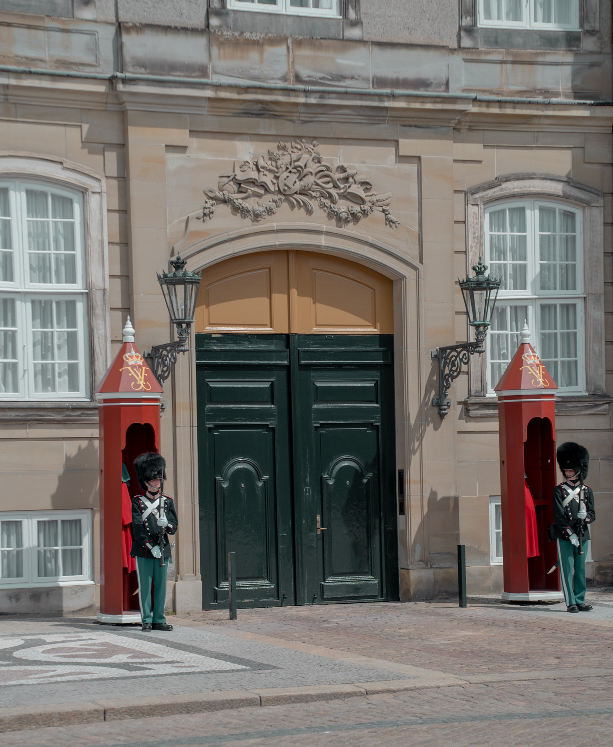 Two guards in front of a large ornate door with decorative elements.