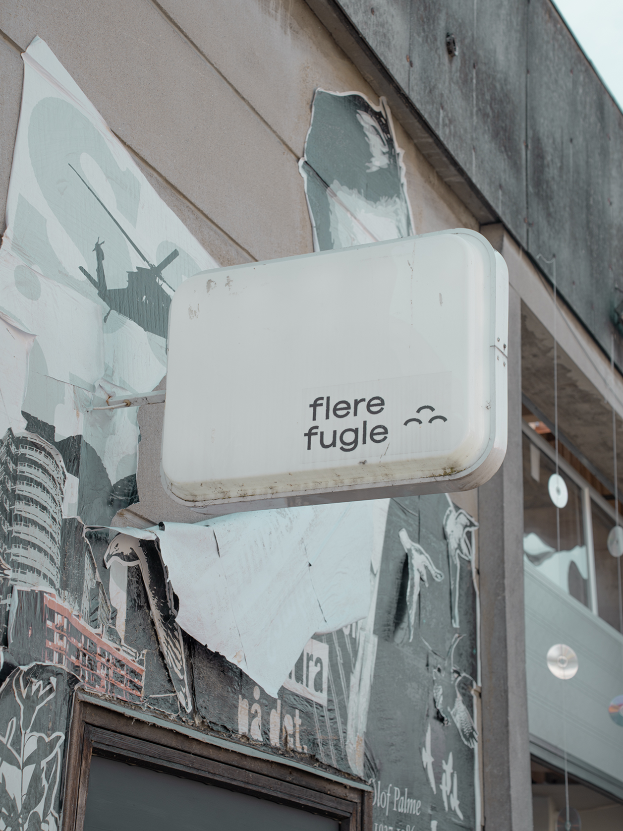 Sign with 'flere fugle' text on a building facade with peeling paint.