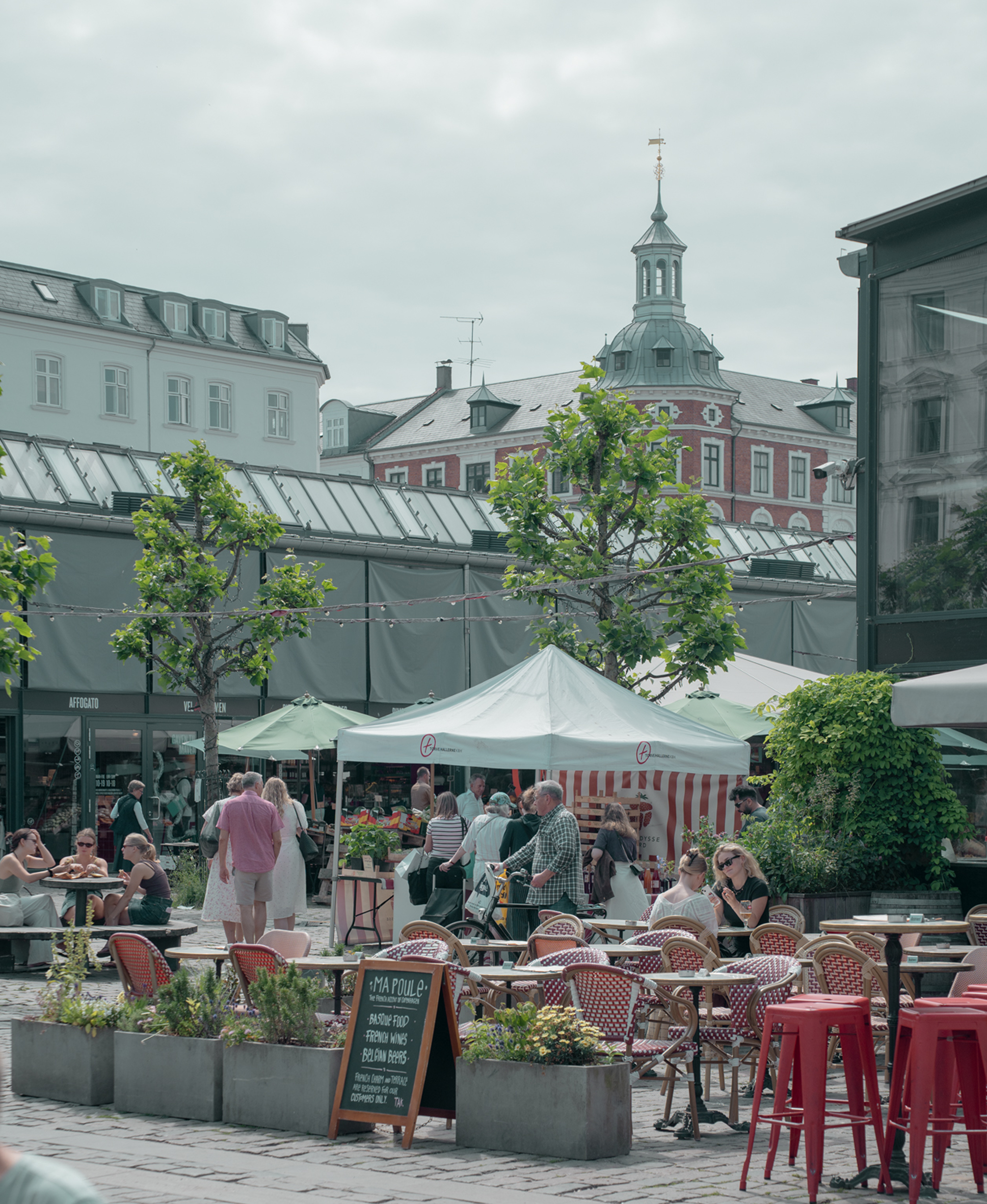 Outdoor cafe with tables, chairs, and people in a city setting.