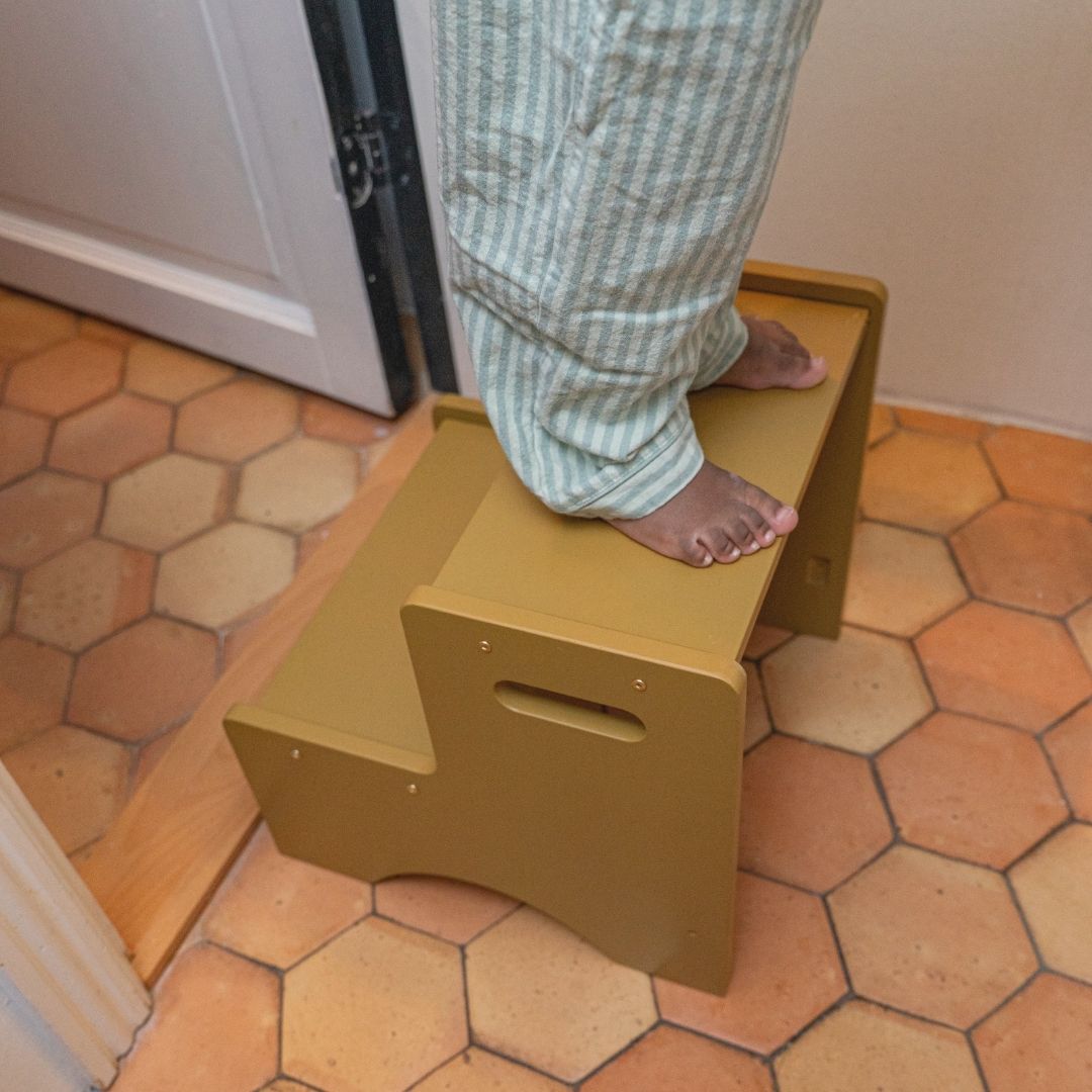 Person stepping onto a yellow step stool on a tiled floor.