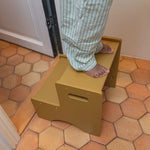 Person stepping onto a yellow step stool on a tiled floor.