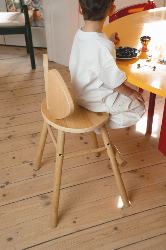 a kid sitting at the dining table on a wooden high chair
