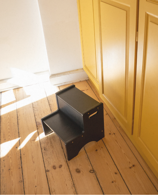 Black step stool on a wooden floor next to a yellow cabinet