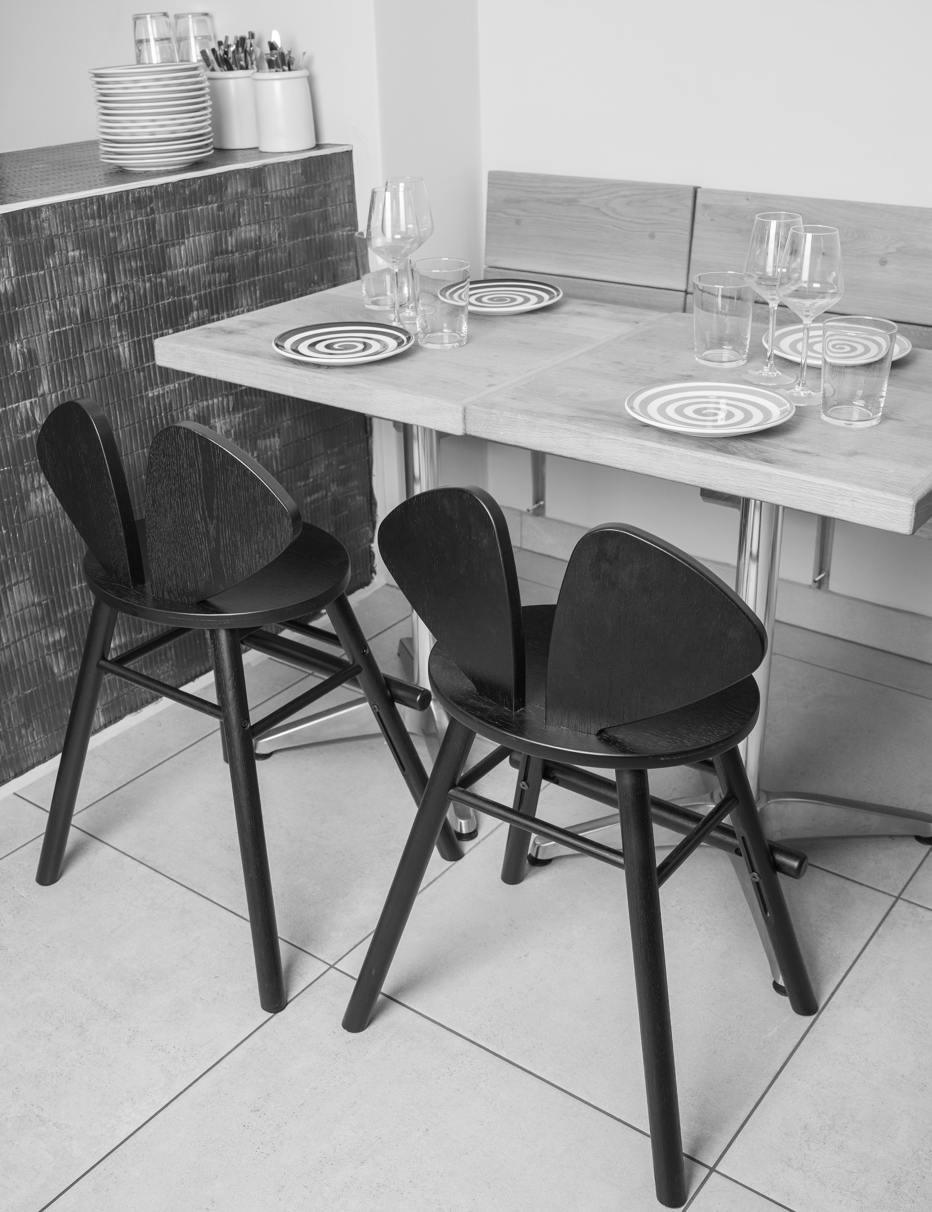 two black kids chairs from the above. Next to them there is a table with the plates