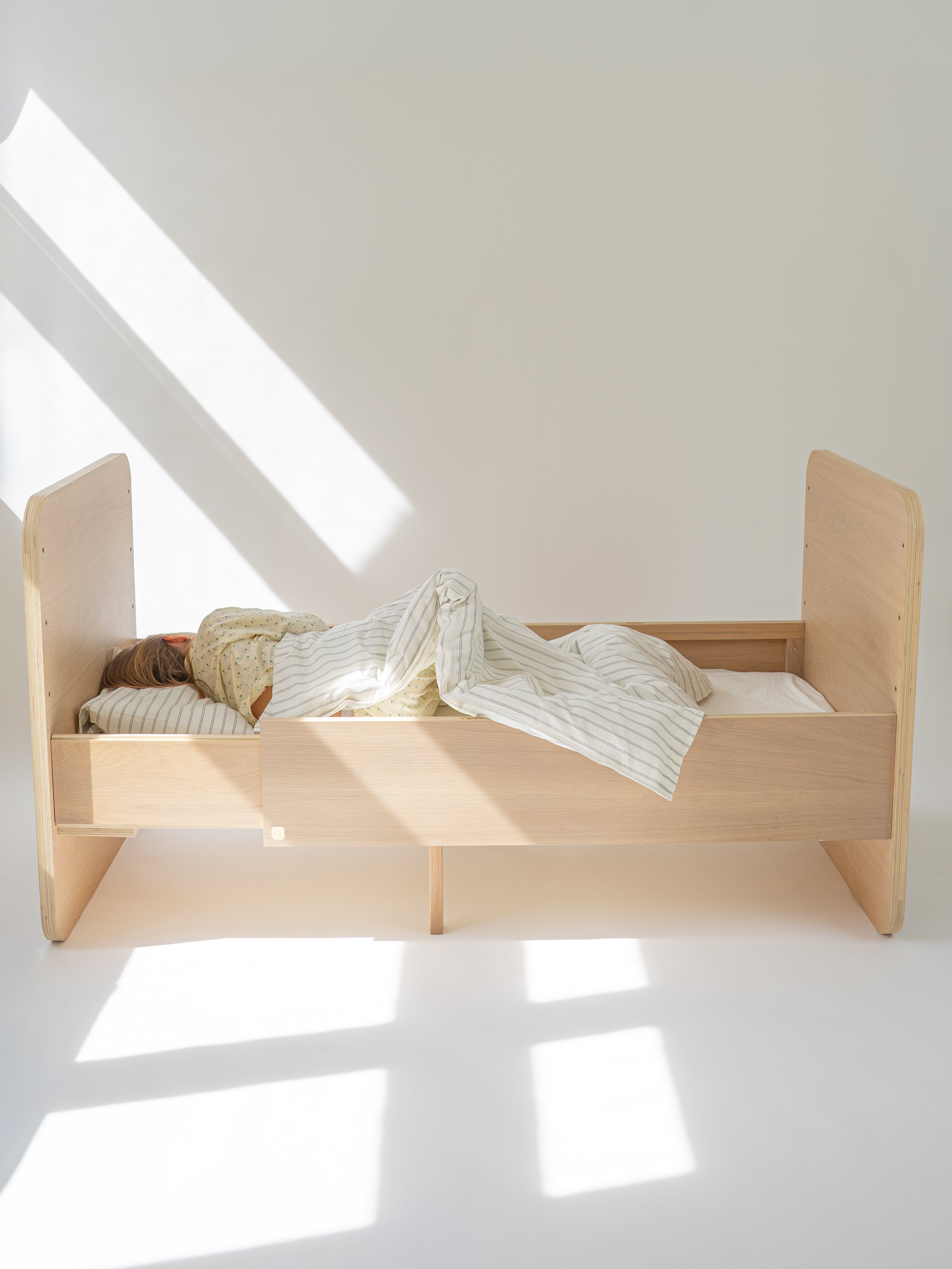 Wooden bed with a child sleeping in a well-lit room with a skylight.