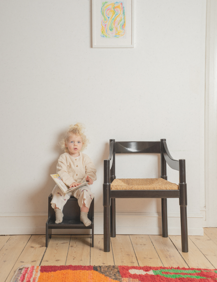 A girl sitting on a black wooden step up stool 