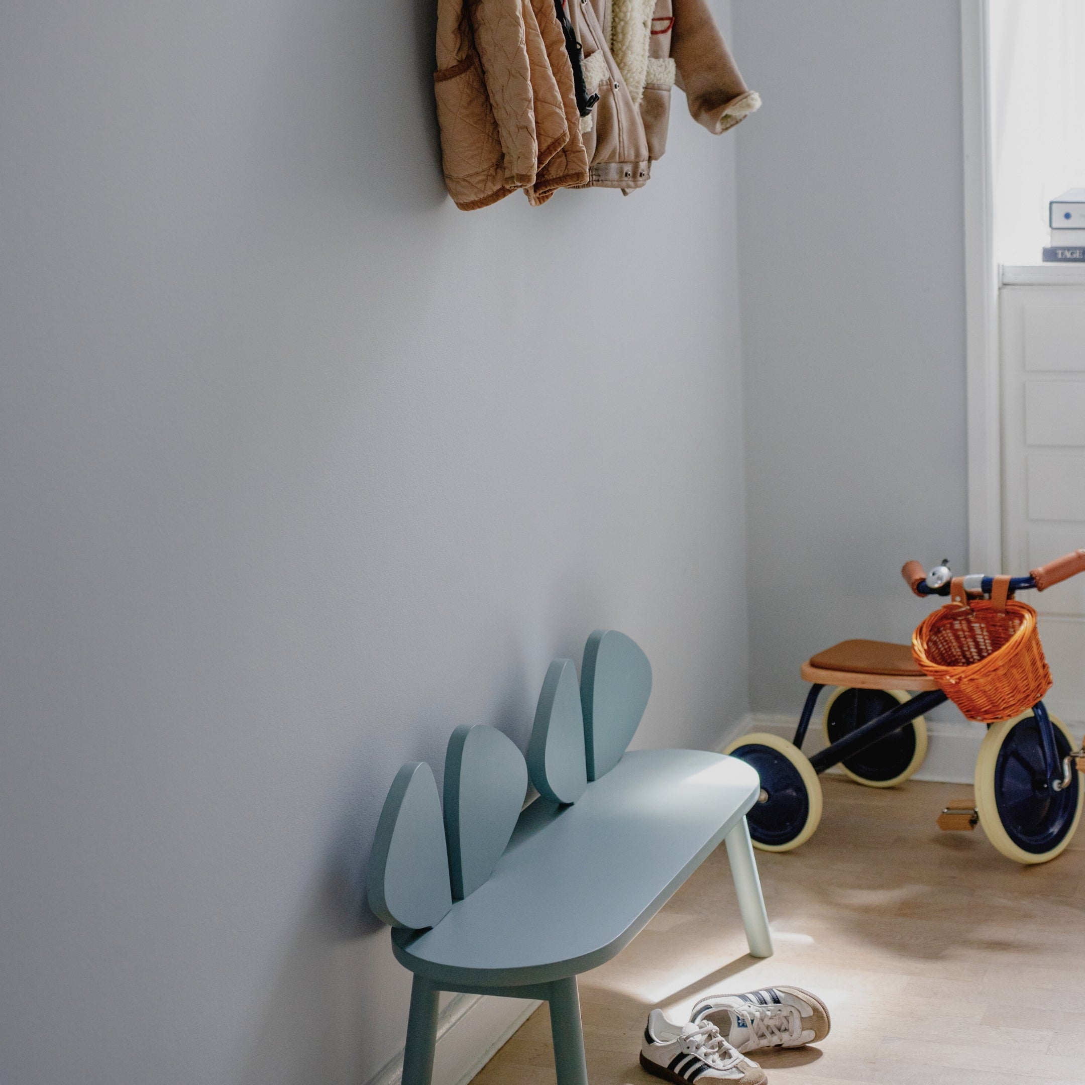 Children's room with a blue chair, tricycle, and shoes on a light wooden floor.