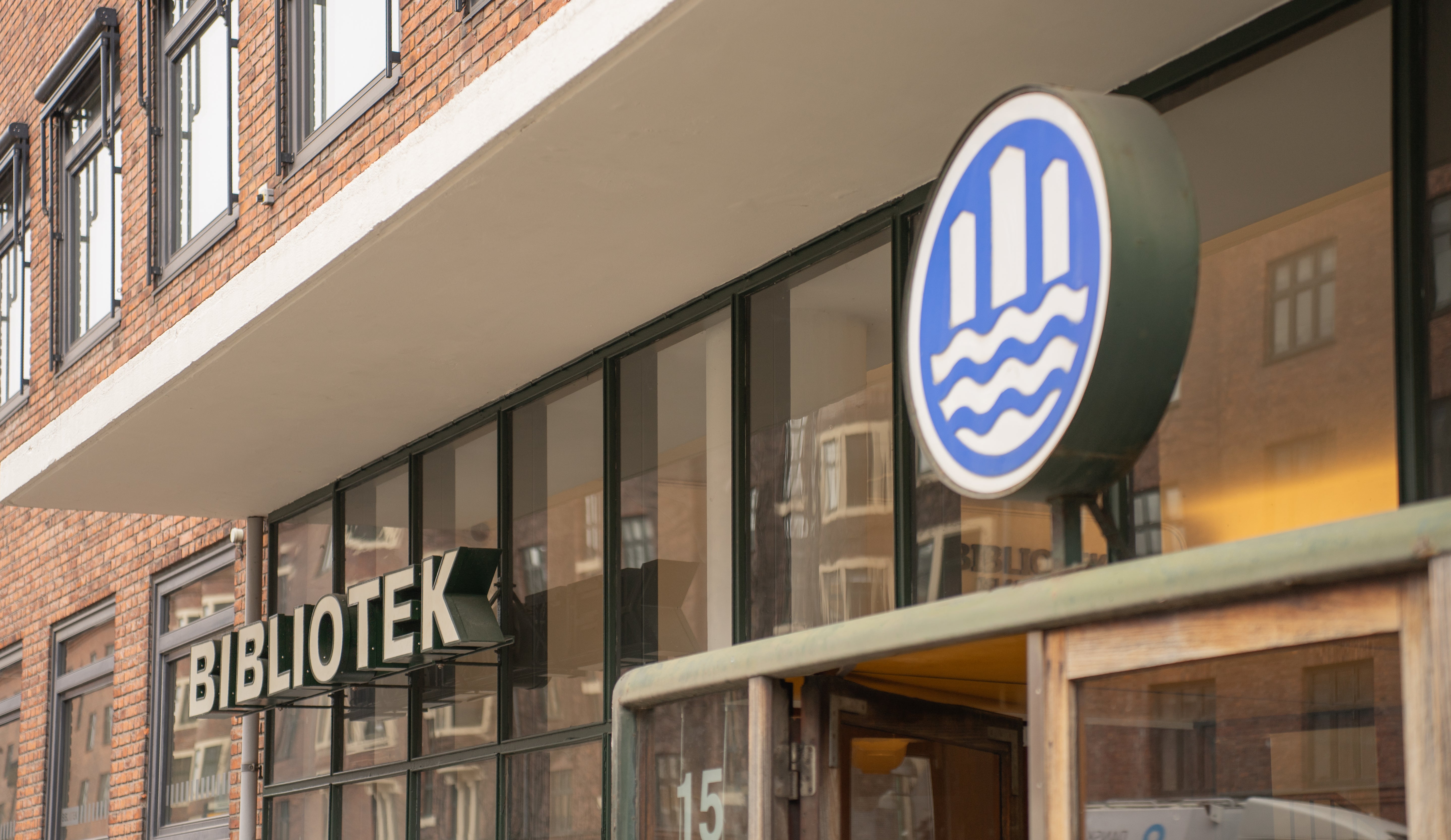 Building exterior with a 'BIBLIOTEK' sign and a circular logo on a brick wall.
