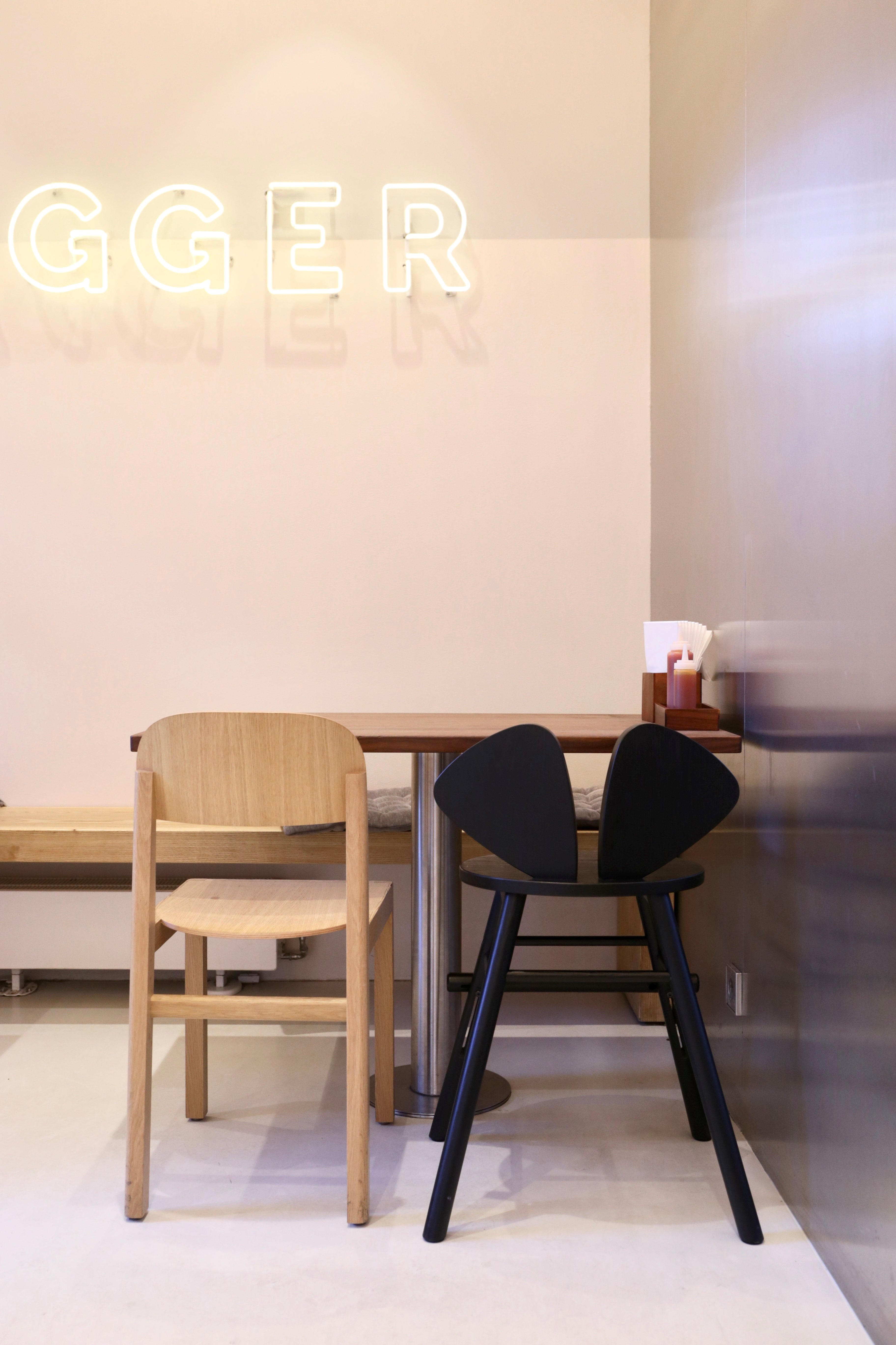 Two chairs, one wooden and one black, in a minimalistic room with a neon sign on the wall.