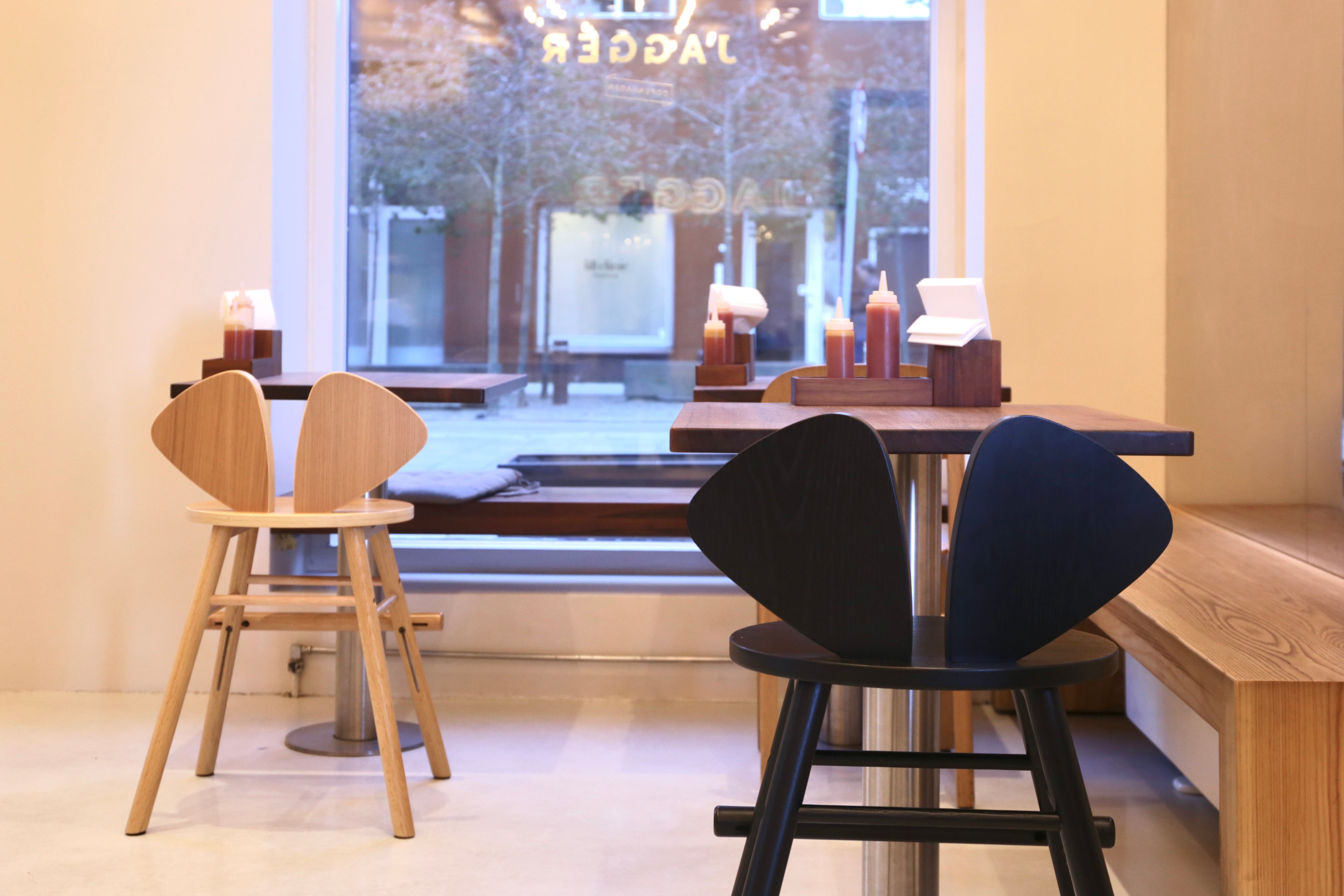 Two stools, one wooden and one black, in a modern interior setting with large windows.