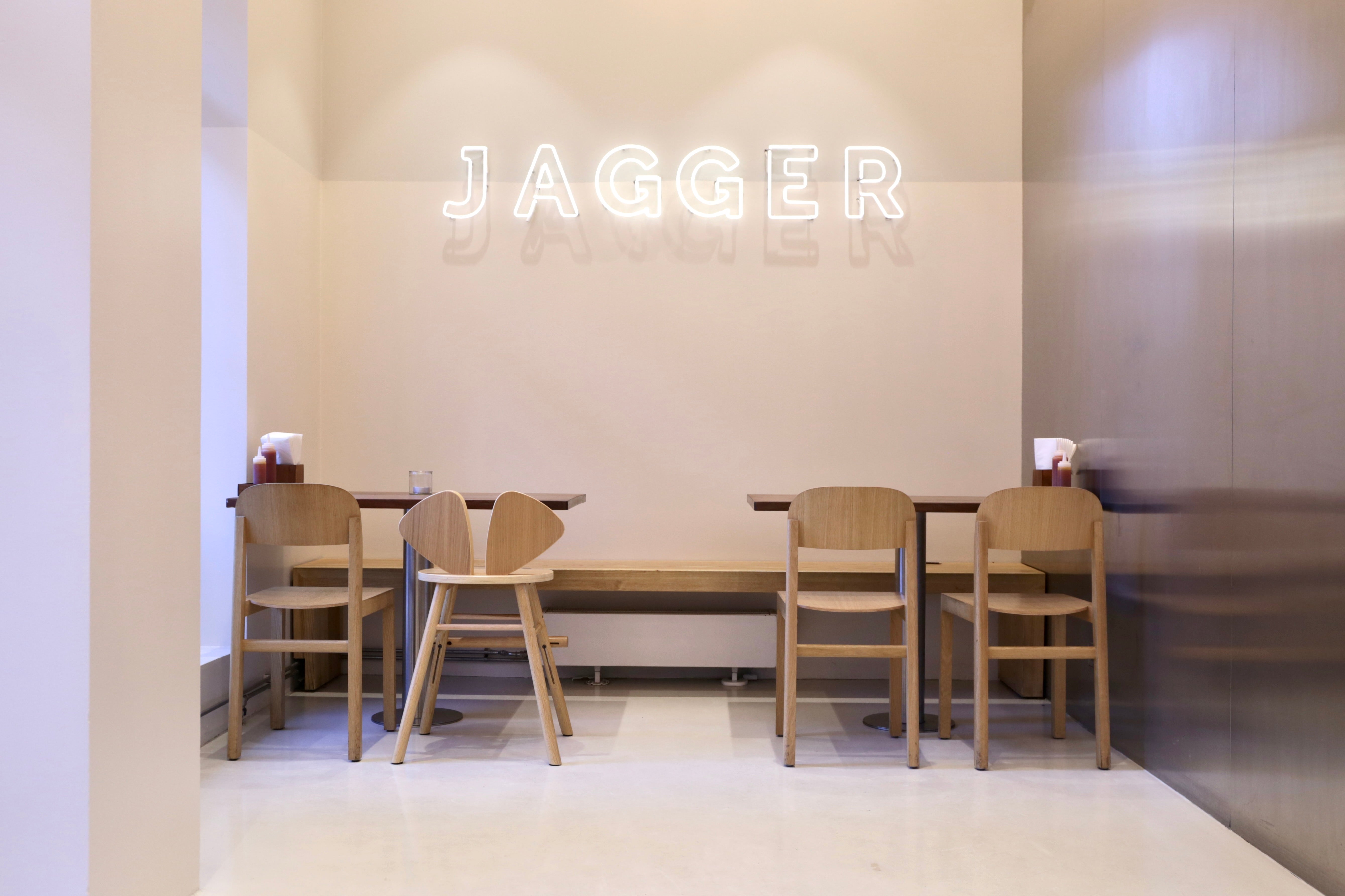 Dining area with wooden chairs and a table, featuring a neon sign with 'Jagger' branding.