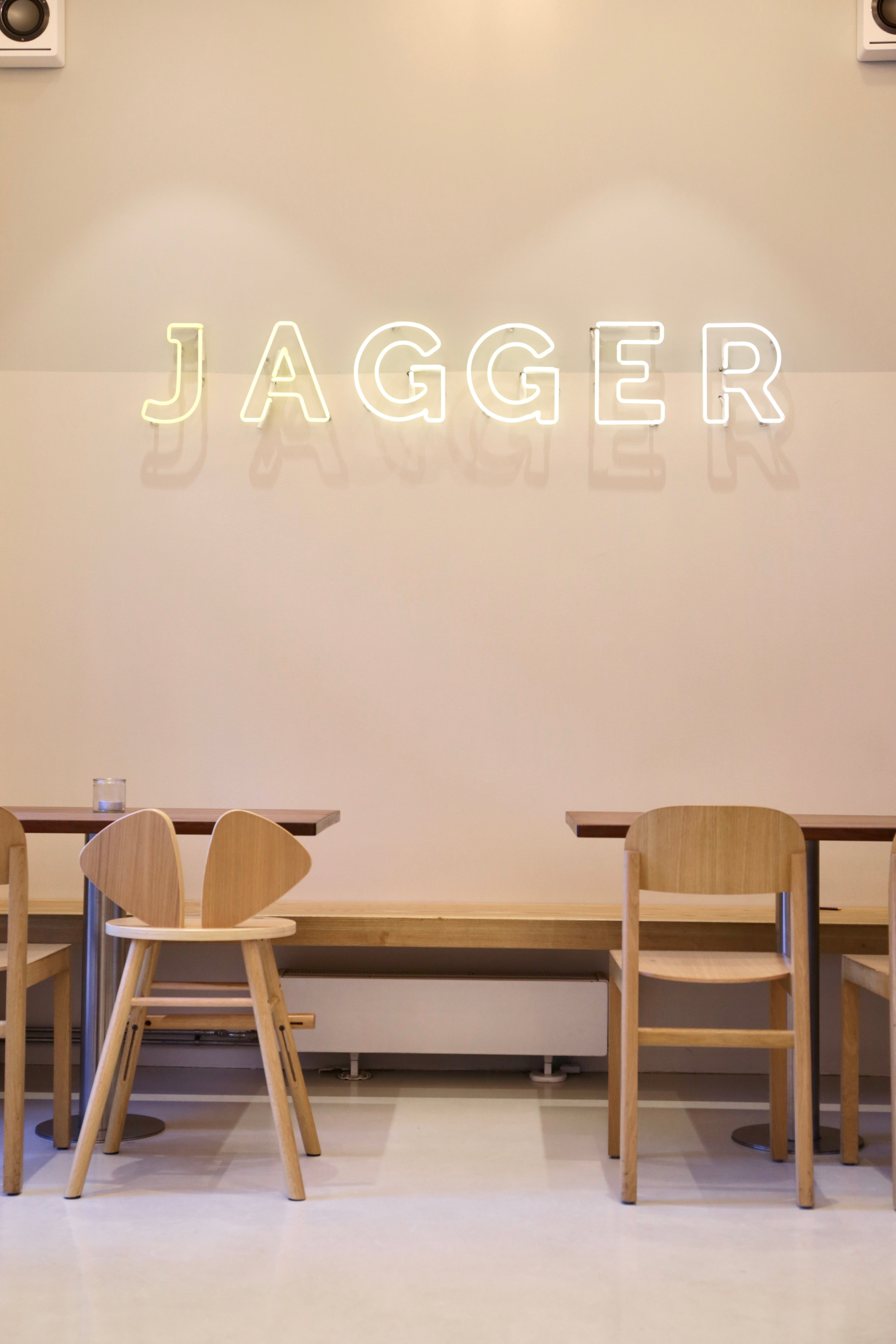Neon sign reading 'Jagger' above a dining area with wooden chairs and tables.