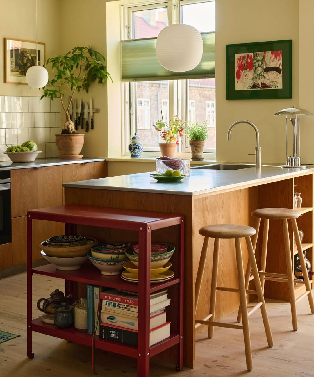 Modern kitchen with a red island shelf, stools, and a window view.