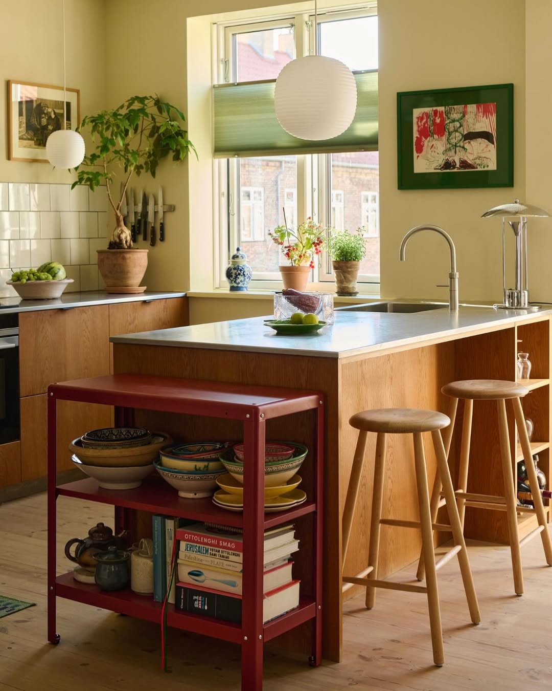 Modern kitchen with a red island shelf, stools, and a window view.