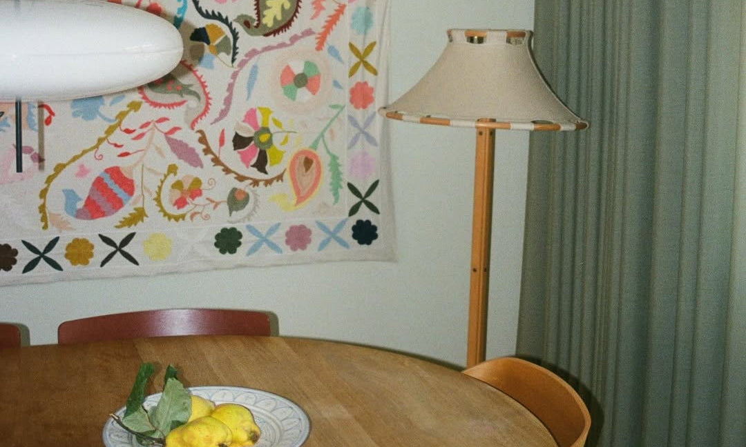 Dining area with a table, chairs, and a colorful tapestry on the wall.