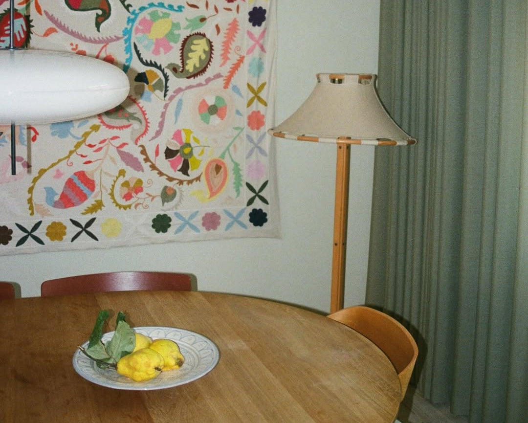 Dining area with a table, chairs, and a colorful tapestry on the wall.