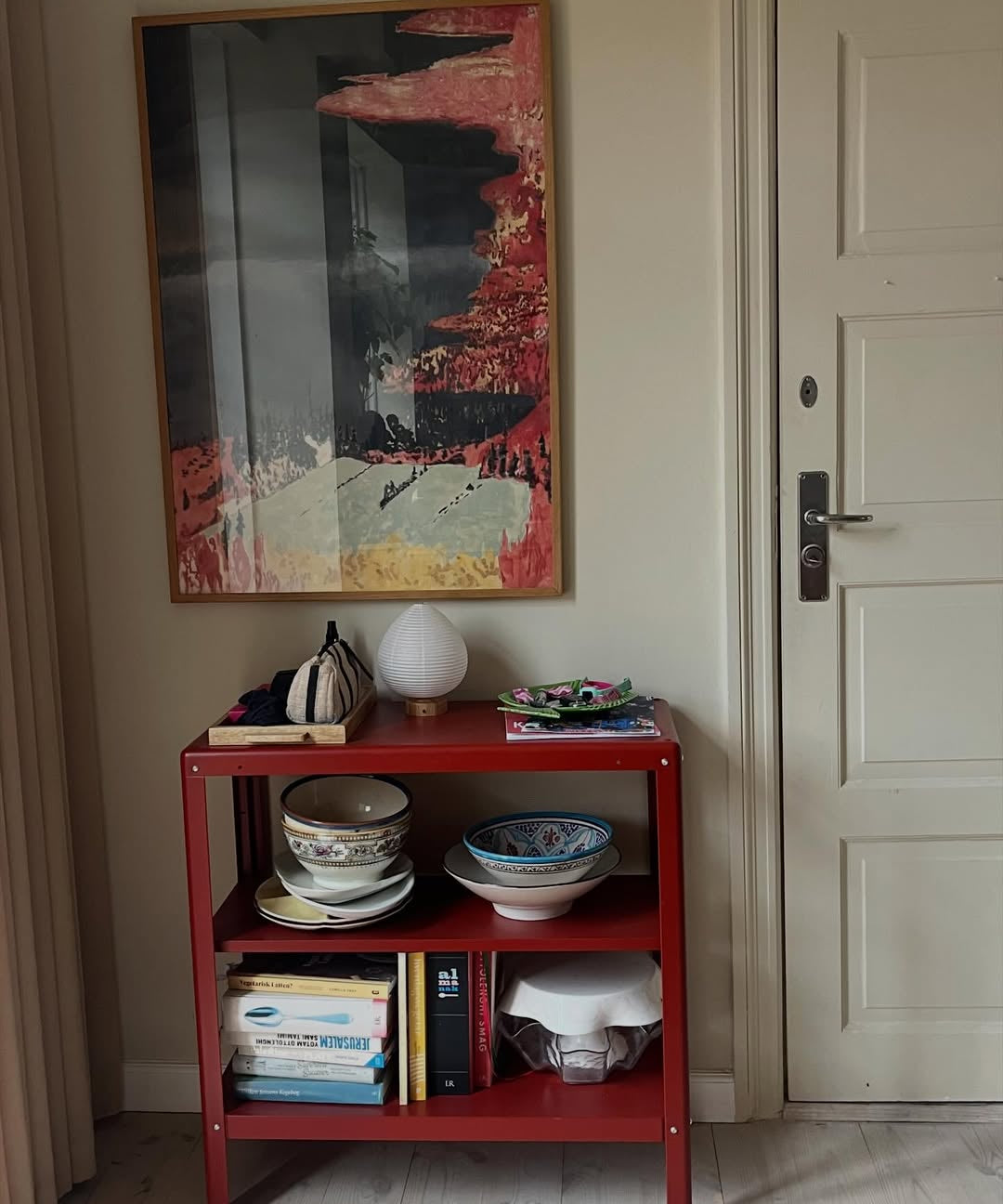 Red shelf with decorative items against a wall with a colorful abstract painting.