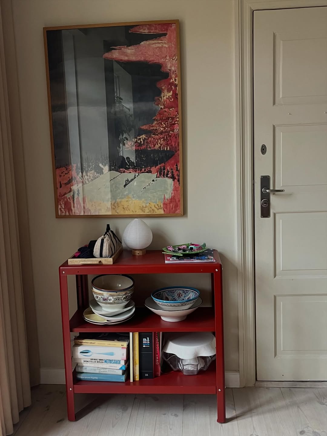 Red shelf with decorative items against a wall with a colorful abstract painting.