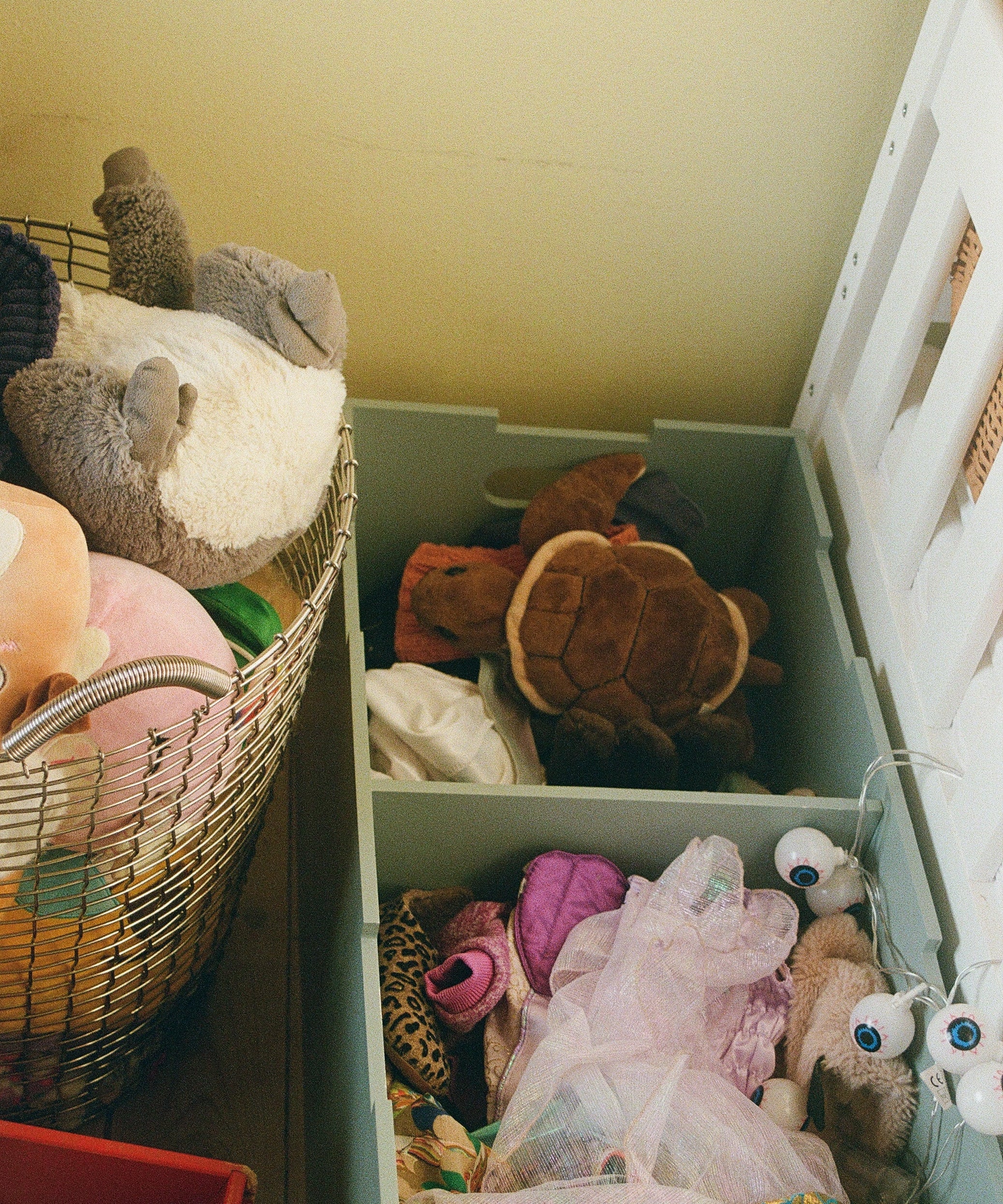 Open drawer filled with various stuffed toys and items on a yellow wall background