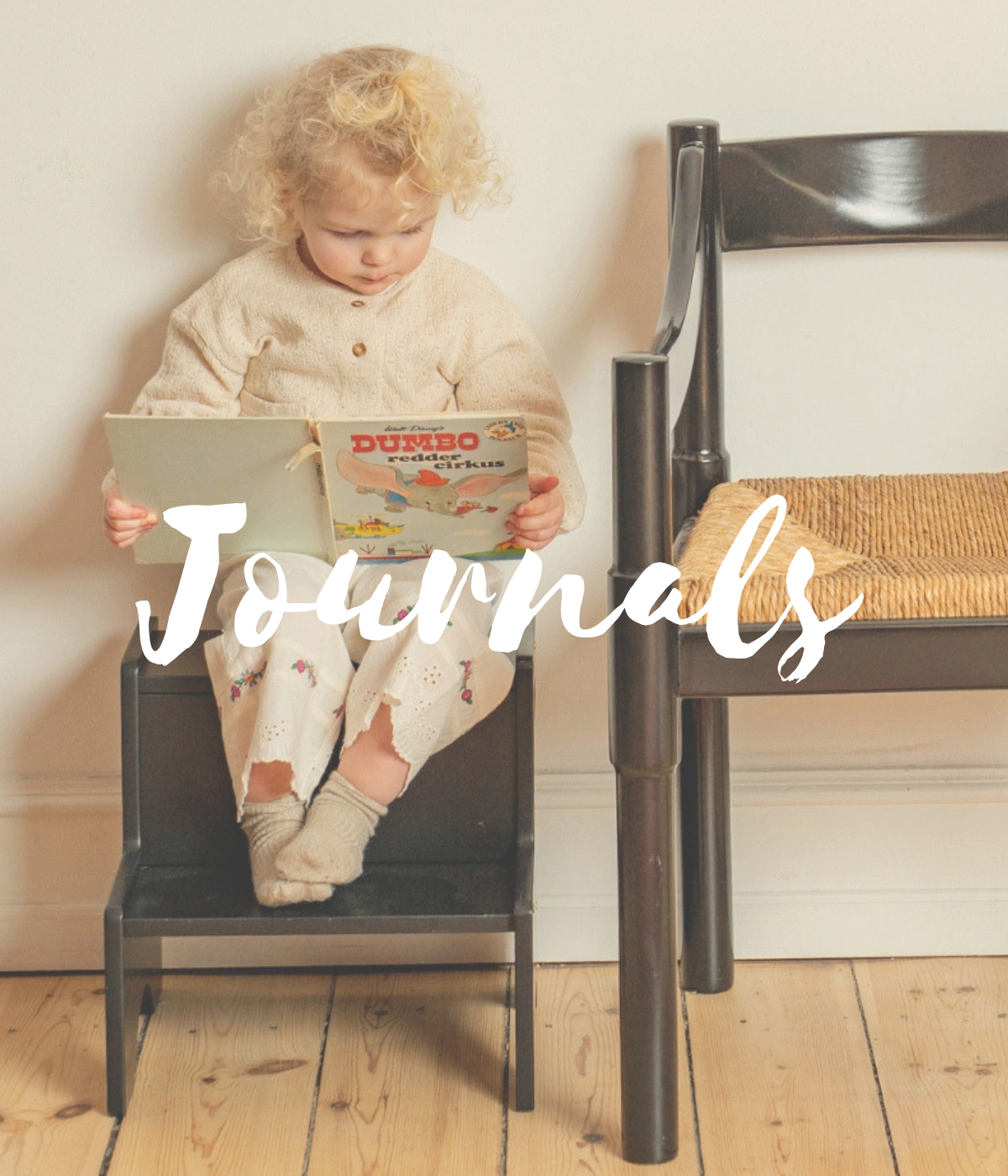 Child sitting on a chair reading a book titled 'Dumbo' with the word 'Journals' overlaid.