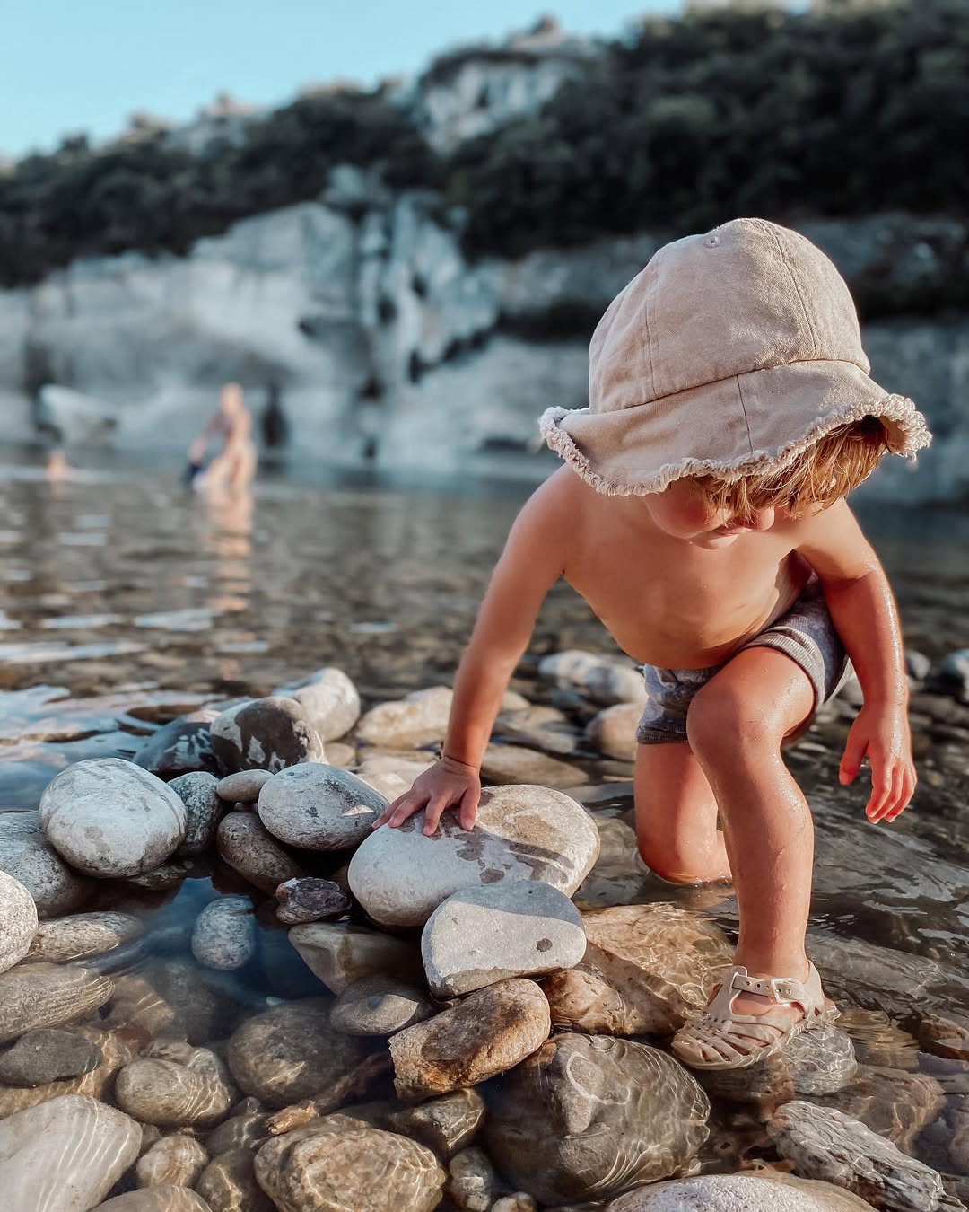 Child playing on a rocky beach with a hat on