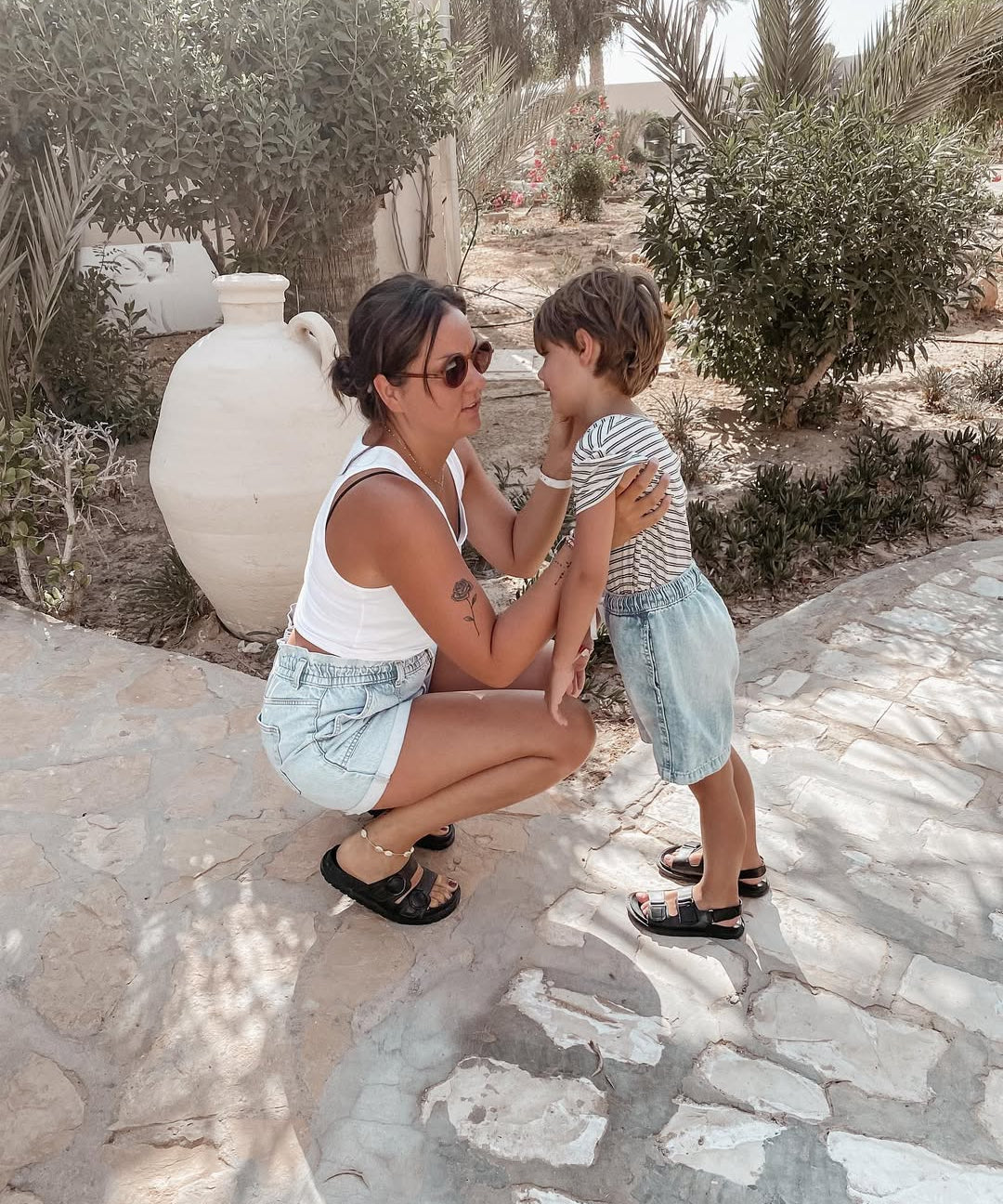 Woman and child sitting on a stone path outdoors with greenery in the background