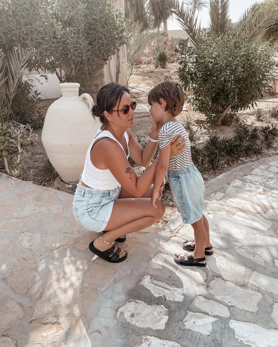 Woman and child sitting on a stone path outdoors with greenery in the background