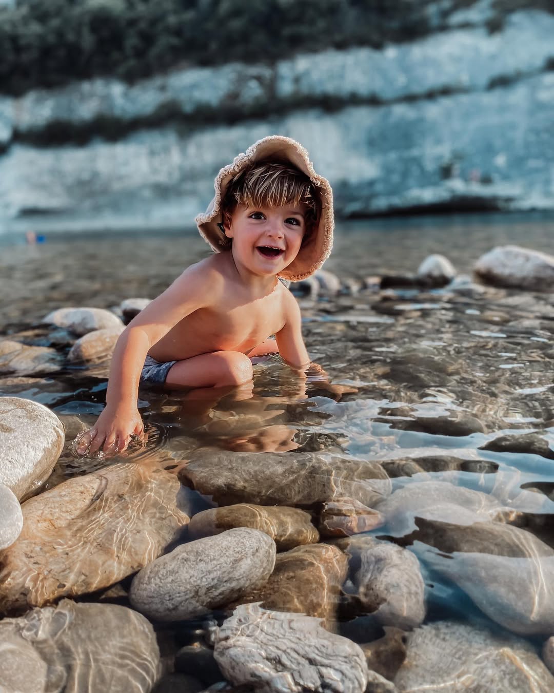 Child playing in water near rocks with a glacier in the background
