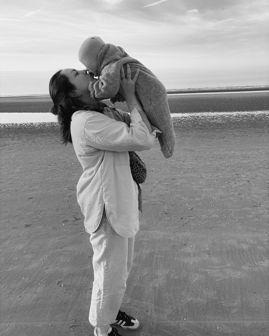 Person holding a child on a beach with a cloudy sky