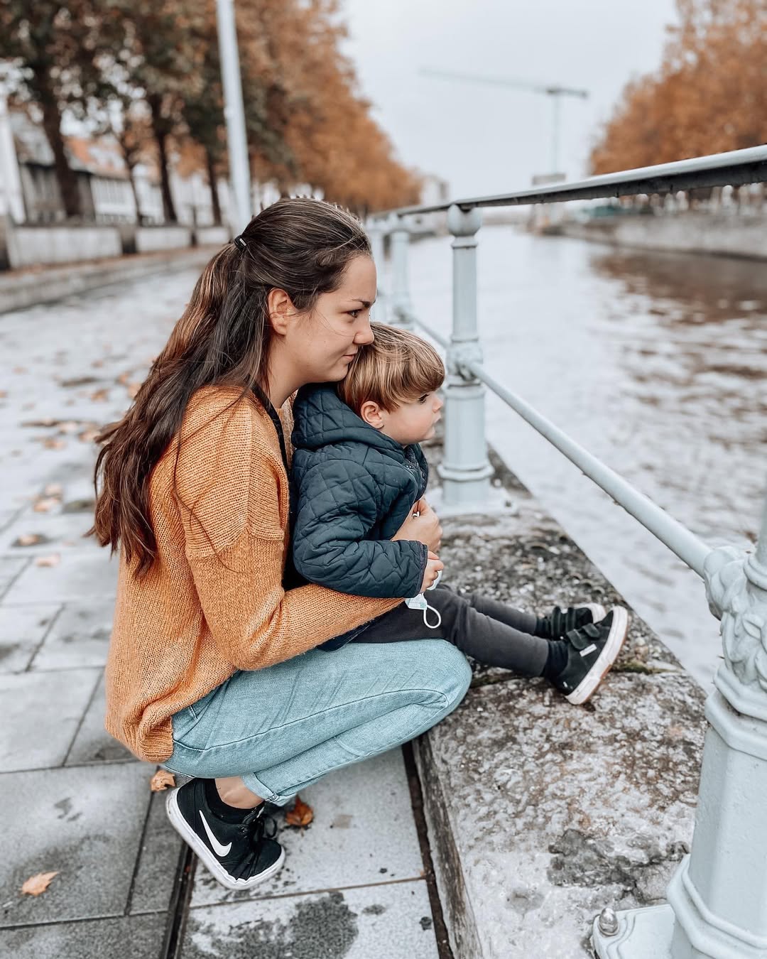 Woman and child sitting on a snowy sidewalk with a railing.