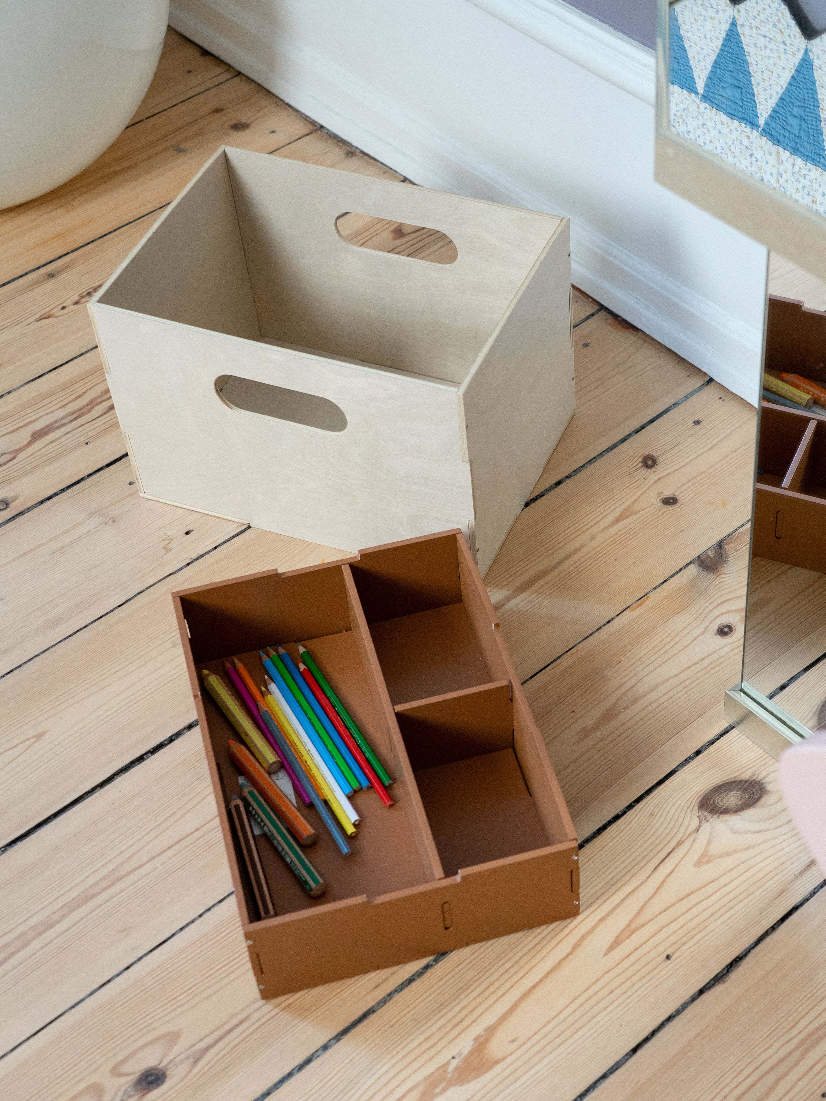 Children's room with storage boxes, colorful pencils, and a pink chair on a wooden floor.
