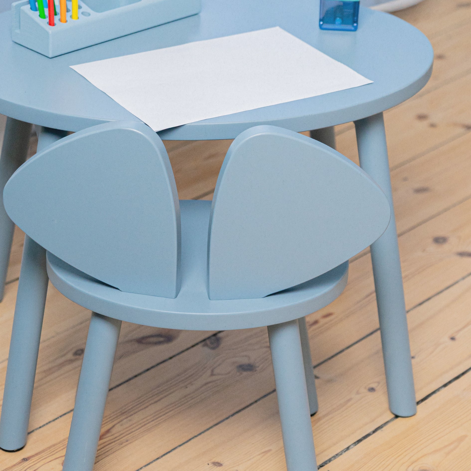 Children's blue table and chair set with art supplies on a wooden floor.