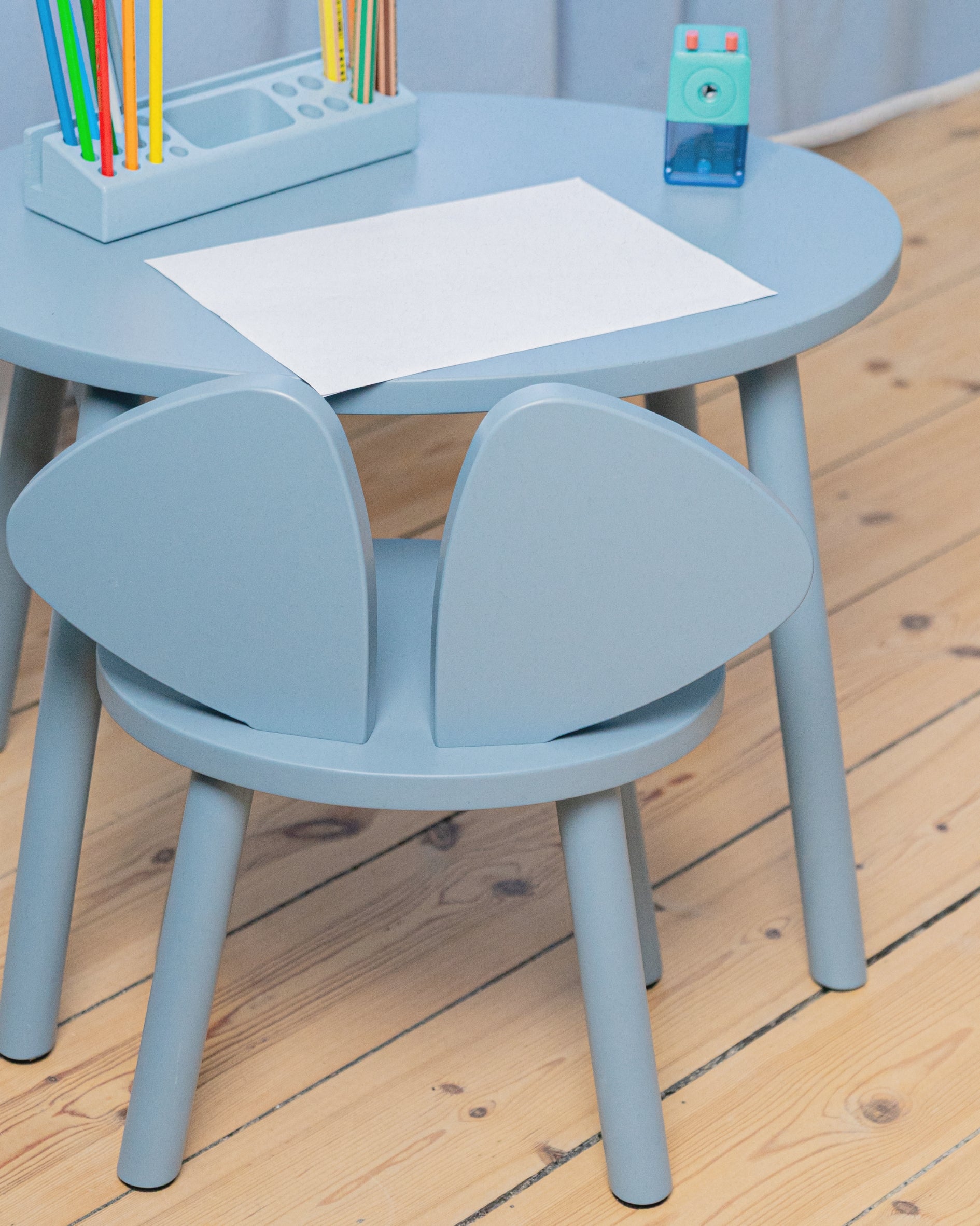 Children's blue table and chair set with art supplies on a wooden floor.