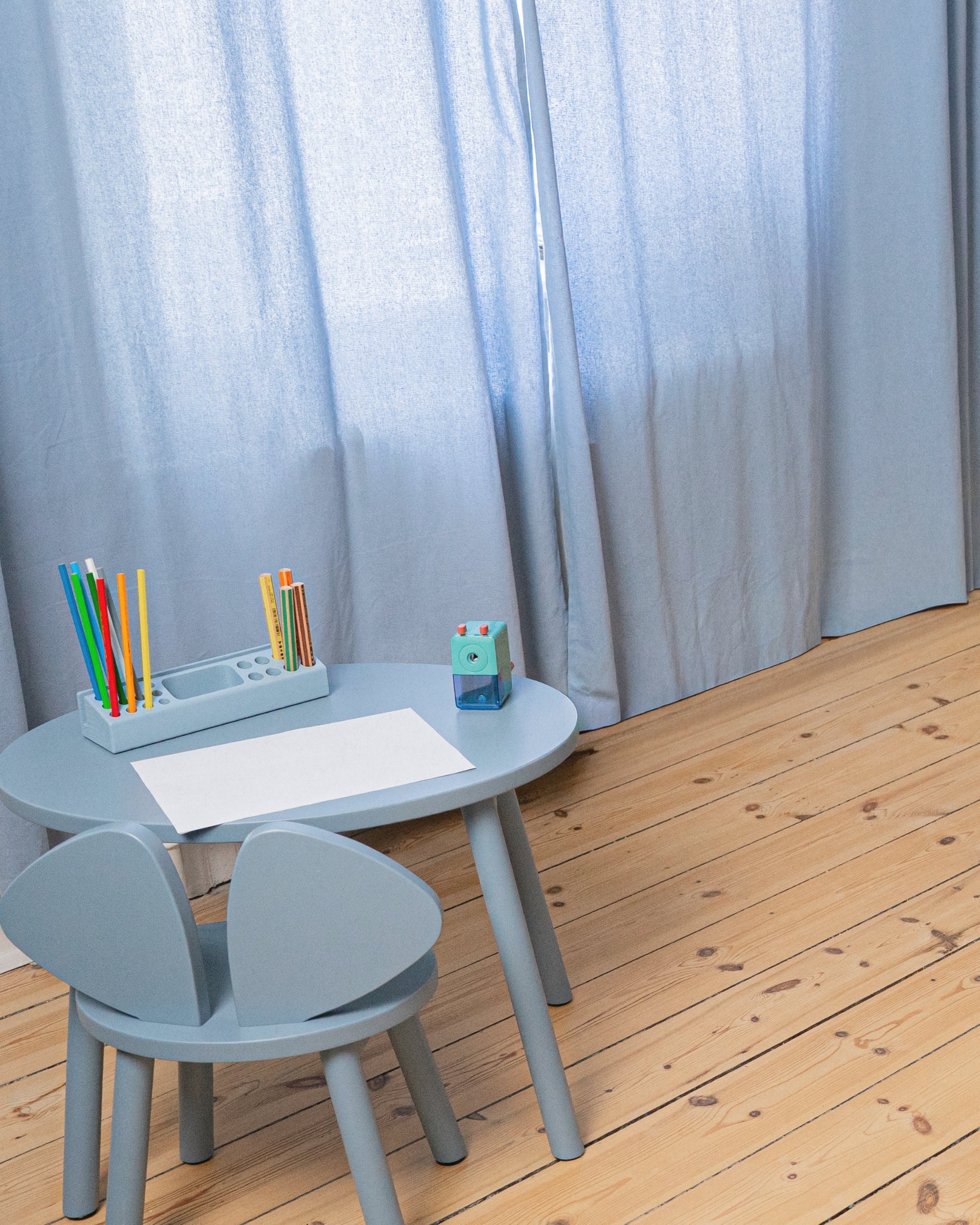 Children's table and chair set with stationery against a light curtain background