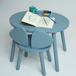 A light blue children's table and chair set with a round table and two matching chairs, styled with drawing accessories on a neutral studio background.